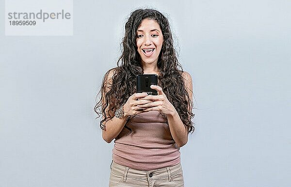 Glücklich und überrascht Mädchen Blick auf eine Förderung auf dem Handy. Lächelnde Frau Texting mit Handy isoliert. Glücklich lateinischen Mädchen mit Handy isoliert