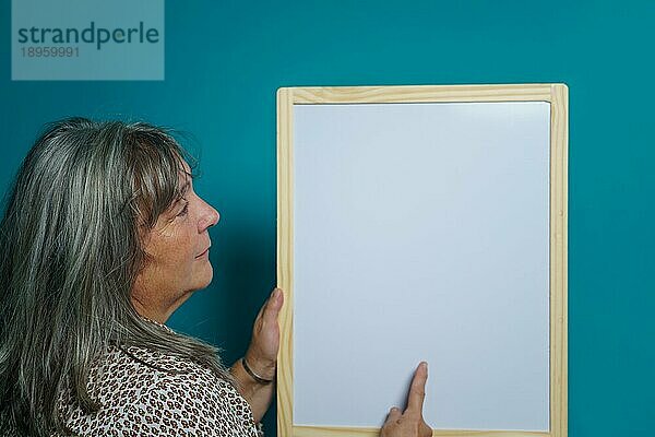 Ältere weißhaarige Frau hält eine weiße Tafel  auf die sie Text klebt