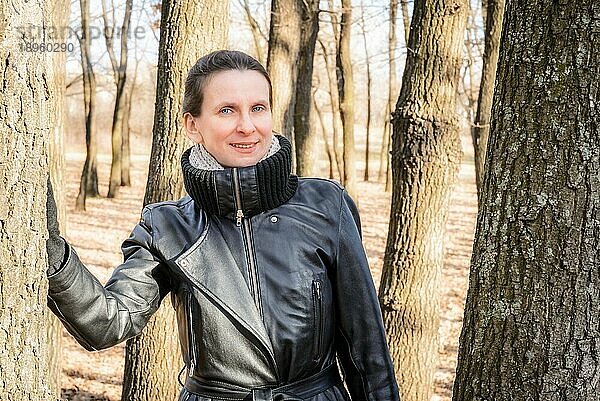 Eine erwachsene Frau in einem schwarzen Ledermantel steht im Eichenwald