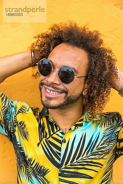 Attraktiver Mann mit Afrohaar im Sommer in einem Palmenhemd auf gelbem Hintergrund