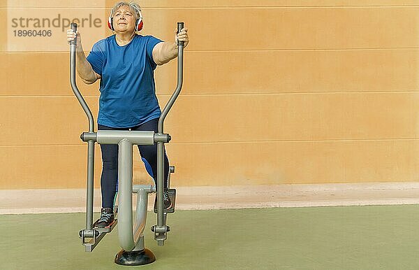 Aktive übergewichtige ältere Frau in Sportkleidung  die auf einem Parkgerät trainiert  während sie über Kopfhörer Musik hört
