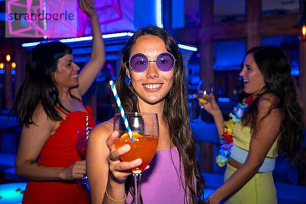 Portrait attraktive Frau stößt an und hat Spaß mit einem Glas Alkohol in einem Nachtclub auf einer Nachtparty