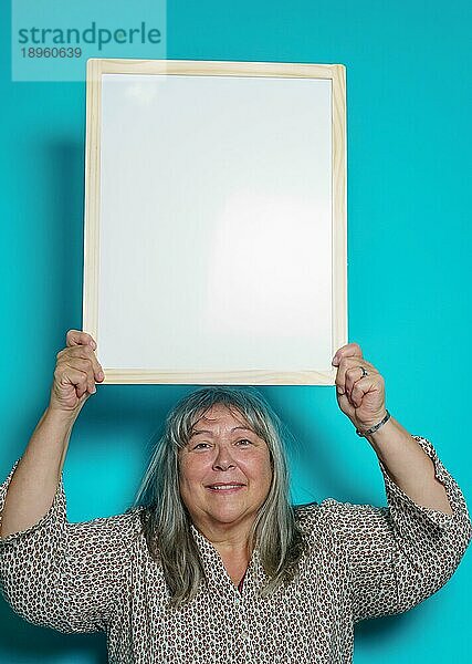 Ältere weißhaarige Frau hält eine weiße Tafel  auf die sie Text klebt