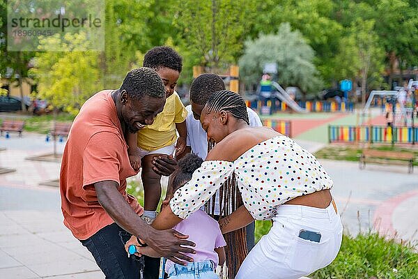 Afrikanische schwarze ethnische Familie mit Kindern auf dem Spielplatz  die sich mit dem Fahrrad umarmen