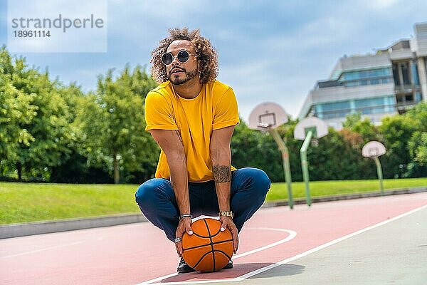 Porträt eines afro haarigen Mannes in einem gelben TShirt mit einem Basketball. Porträt auf einem Basketballplatz in der Stadt