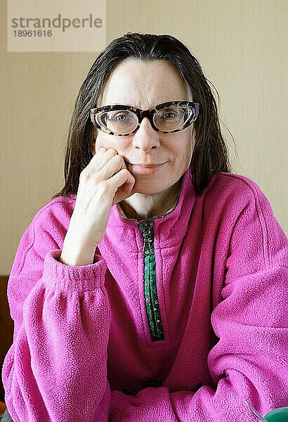Eine lächelnde reife Frau mit Brille  die einen rosa Pullover trägt  am Morgen nach dem Frühstück