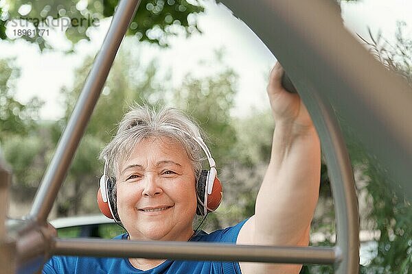 Aktive fettleibige ältere Frau in Sportkleidung  die auf einem Fitnessgerät im Park trainiert  während sie über ihre Kopfhörer Musik hört