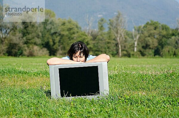 Glückliche Frau  die sich an einem sonnigen Tag auf dem Feld an einen Fernseher lehnt