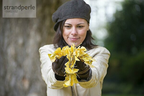 Glückliche Frau mit Hut und gelben Herbstblättern