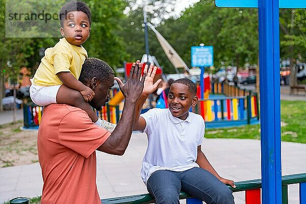 Afrikanischer schwarzer ethnischer Vater winkt mit seinen Kindern auf dem Spielplatz des Stadtparks