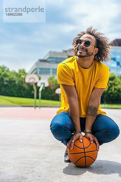 Porträt eines afro haarigen Mannes in einem gelben TShirt mit einem Basketball. Porträt in der Stadt lächelnd im Sommerurlaub