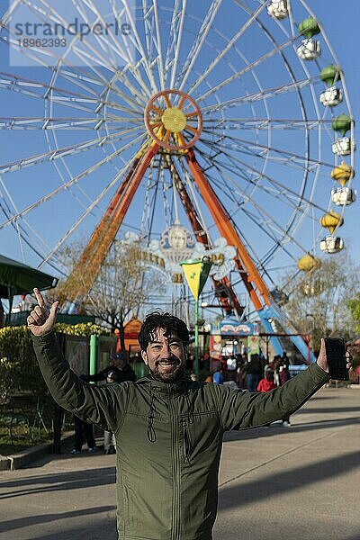 Porträt eines Latinomannes in einem Vergnügungspark  der glücklich mit dem Riesenrad im Hintergrund posiert