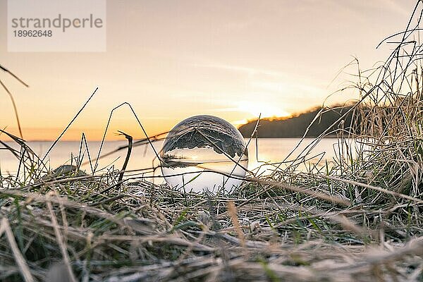 Kristallkugel im gefrorenen Gras an einem See bei Sonnenaufgang an einem kalten Tag
