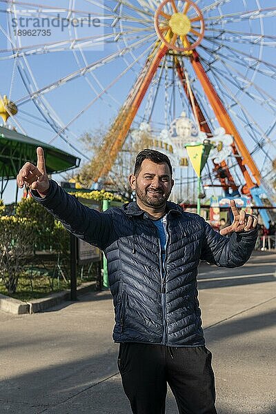 Porträt eines Latinomannes in einem Vergnügungspark  der glücklich mit dem Riesenrad im Hintergrund posiert