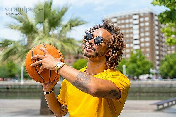 Porträt eines afrohaarigen Mannes im gelben TShirt mit einem Basketball. Porträt in der Stadt