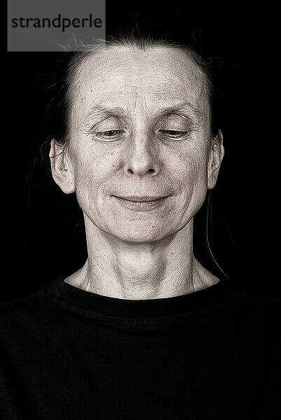 Porträt einer attraktiven erwachsenen Frau  die nach unten schaut und sanft lächelt