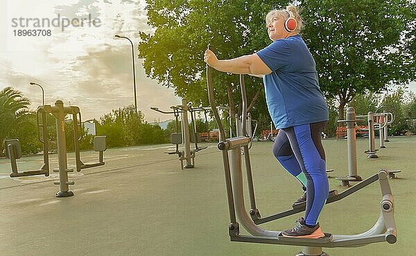 Aktive übergewichtige ältere Frau in Sportkleidung  die auf einem Parkgerät trainiert  während sie über Kopfhörer Musik hört