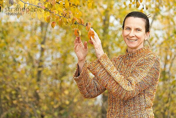 Eine lächelnde erwachsene kaukasische Frau pflückt orangefarbene Apfelblätter im Herbst