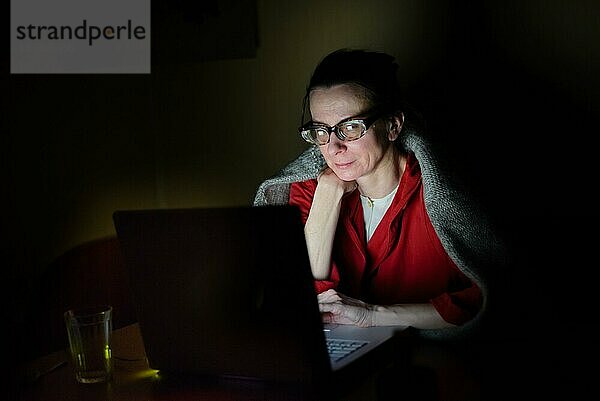 Eine ältere Frau  die an einem kalten Winterabend im Dunkeln einen Computer benutzt
