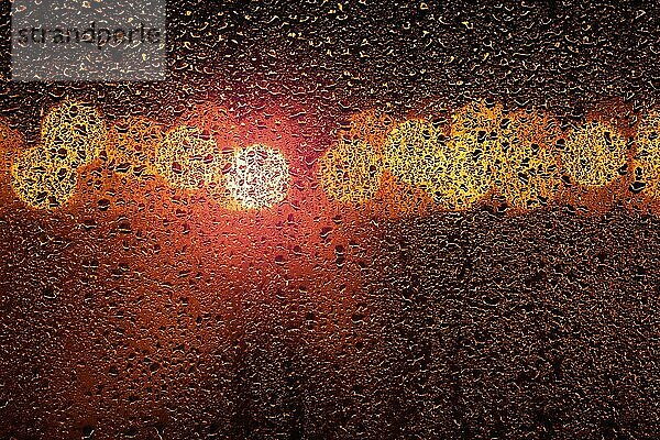 Regen auf ein Fenster mit großen Stadt Bokeh Lichter in orange und violetten Farben