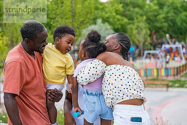 Afrikanische schwarze ethnische Familie mit Kindern auf dem Spielplatz  die sich nach der Schule umarmen und küssen