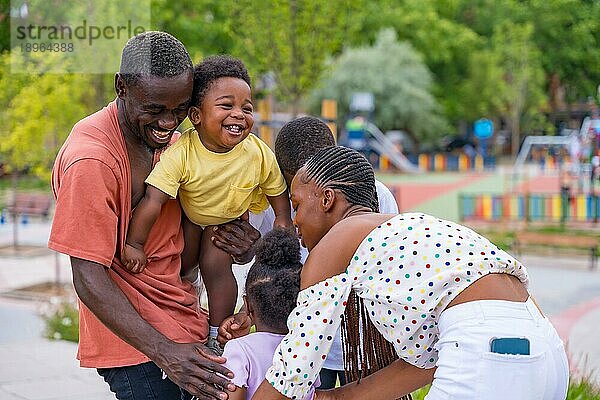 Afrikanische schwarze ethnische Familie mit Kindern auf dem Spielplatz  die sich nach der Schule umarmen