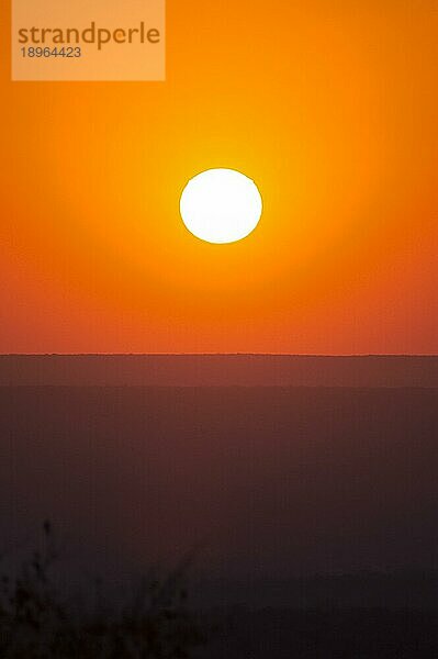 Großer roter Sonnenuntergang über Silhouetten von Hügeln in einer Schlucht im Spätsommer