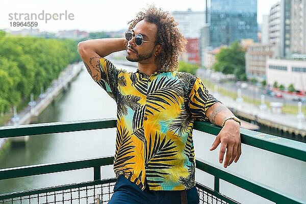Past eines attraktiven Mannes mit Afrohaar im Sommer  der ein Palmenhemd trägt  mit der Stadt im Hintergrund  der seinen Urlaub genießt