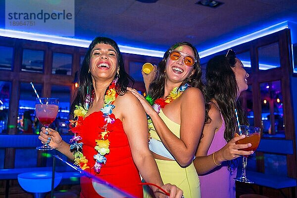 Weibliche Freunde in einem Nachtclub tanzen mit Gläsern von Alkohol lächelnd auf einer Nachtparty im Sommerurlaub