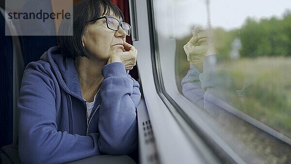 Ältere Dame mit Brille reist im Zug und schaut aus dem Fenster  das sich im Glas spiegelt