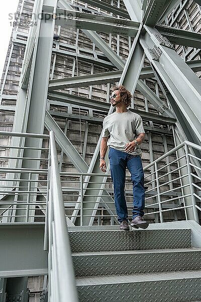 Junger Mann mit Afro Haare tragen Sonnenbrille zu Fuß die Treppe hinunter in der Stadt  urbane Mode cooles Konzept eines Hipster Kerl mit stilvollen