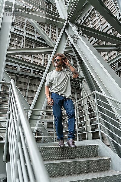 Junger Mann mit Afro Haare tragen Sonnenbrille zu Fuß die Treppe hinunter in der Stadt  urbane Mode cooles Konzept eines Hipster Kerl mit stilvollen