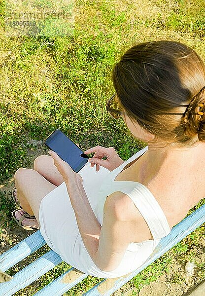 Eine ältere Frau sitzt auf einer Waldbank und benutzt ihr Smartphone  um eine Textnachricht zu versenden