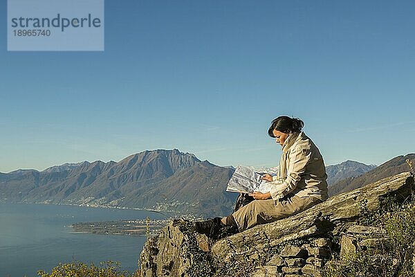 Frau entspannt sich auf einem Berggipfel und liest eine Karte  im Hintergrund der Lago Maggiore  Tessin  Schweiz  Europa