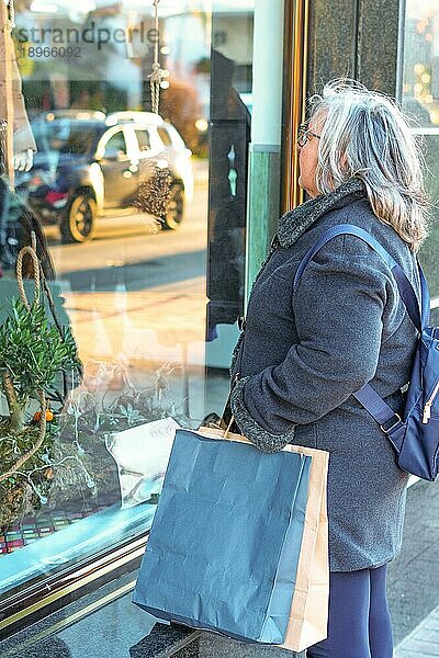 Ronda  Málaga  Spanien Ältere Frau mit weißem Haar und Mantel und Einkaufstüten schaut in ein Schaufenster