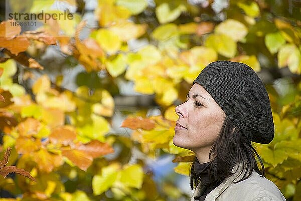 Glückliche Frau mit Hut im Profil mit Herbstblättern