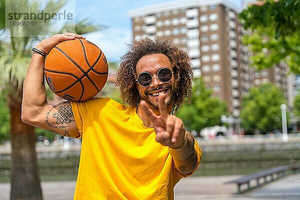 Porträt eines afro haarigen Mannes in einem gelben TShirt mit einem Basketball. Porträt in der Stadt lächelnd im Sommerurlaub