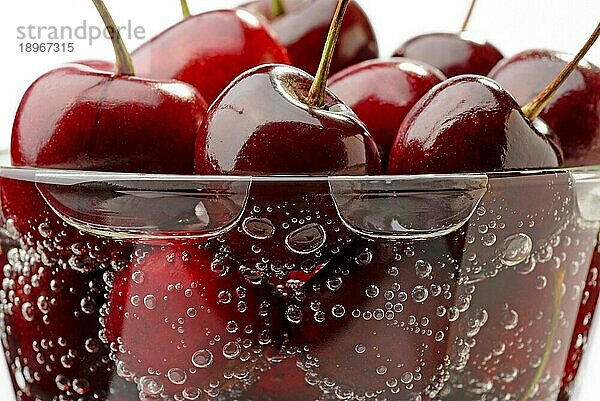 Makroaufnahme von frischen und natürlichen roten Kirschen in einem Glas mit Wasser und Blasen