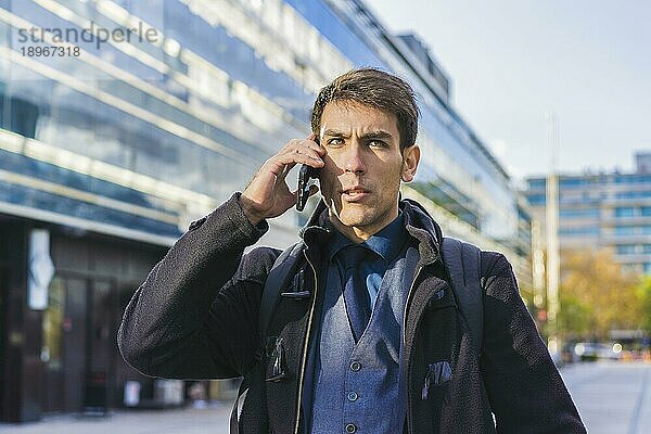 Ein gutaussehender Geschäftsmann  der in der Nähe seines Büros mit dem Handy telefoniert. Raum kopieren