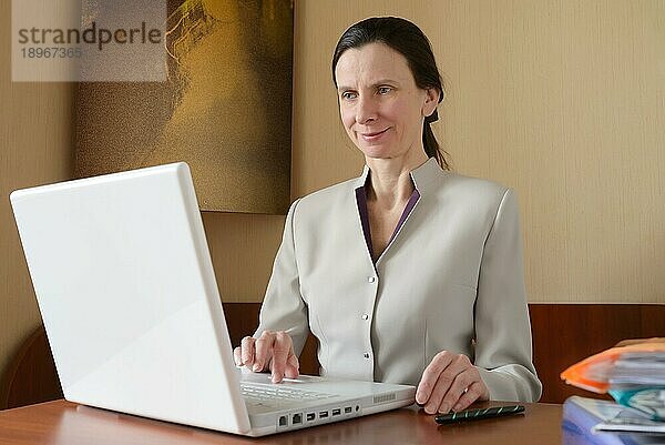 Eine elegante Geschäftsfrau arbeitet mit einem Laptop. Sie ist zufrieden mit ihrer Arbeit