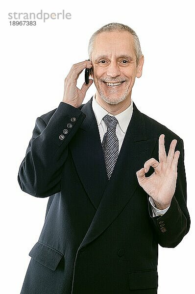 Ein freundlicher Geschäftsmann lächelt auf dem Handy und zeigt das Okay Zeichen mit der Hand