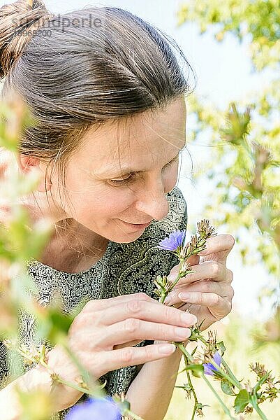 Eine ältere Frau schnuppert an einer blaün Blume im Park an einem warmen Sommertag