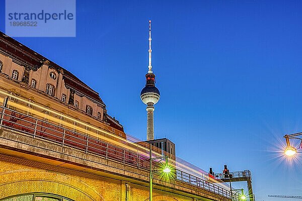 Der ikonische Berliner Fernsehturm in der Abenddämmerung mit einem bewegungsunscharfen Nahverkehrszug