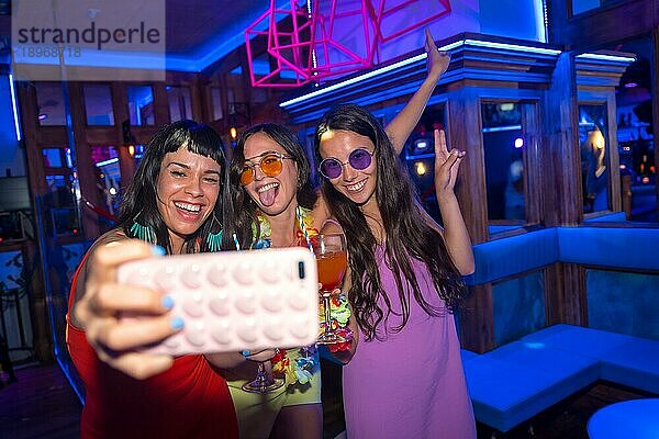 Lächelnde Freunde mit Gläsern Alkohol in einem Nachtclub  die ein Selfie auf einer Nachtparty machen
