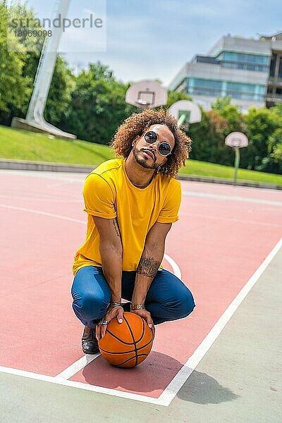 Porträt eines afrohaarigen Mannes im gelben TShirt mit einem Basketball. Porträt in der Stadt