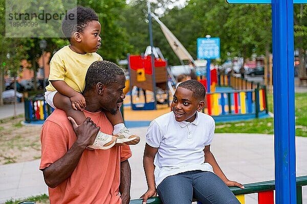 Afrikanischer schwarzer ethnischer Vater im Gespräch mit seinen Kindern auf dem Spielplatz des Stadtparks