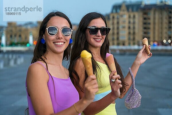 Junge Freundinnen essen lächelnd Eis im Sommerurlaub am Strand