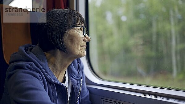 Ältere Dame mit Brille reist im Zug und schaut aus dem Fenster