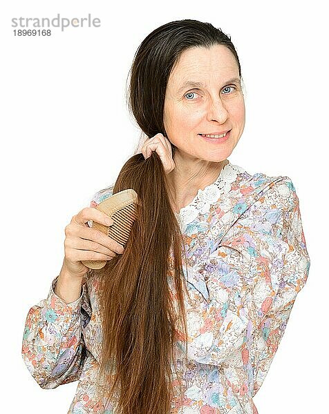 Erwachsene Frau kämmt langes braunes Haar mit einem Holzkamm  vor weißem Hintergrund