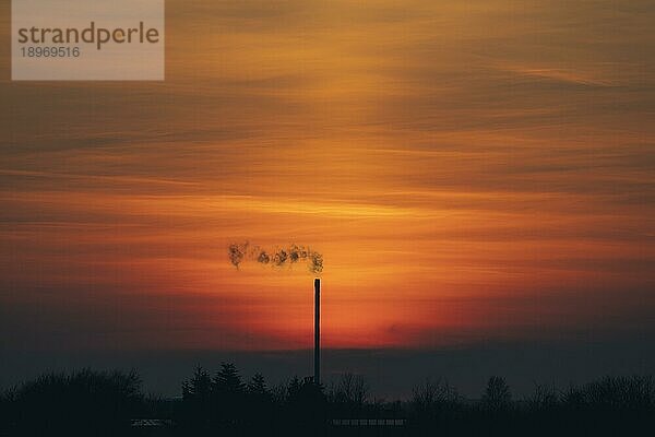 Rauch aus einem Schornstein in einem schönen Sonnenuntergang mit industriellen Silhouetten